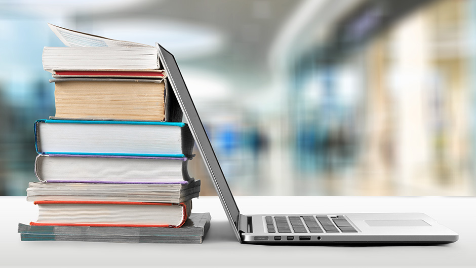 Pile of books and an open laptop on a table