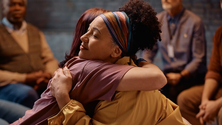 two women hugging at a 12 step type meeting
